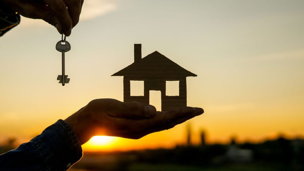 sillouette of house and person holding a key with sunset behind